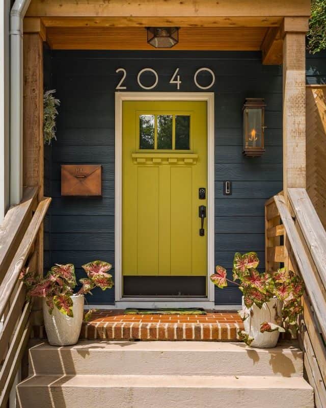 Bright yellow front door with house number 2040, surrounded by potted plants and wooden accents.
