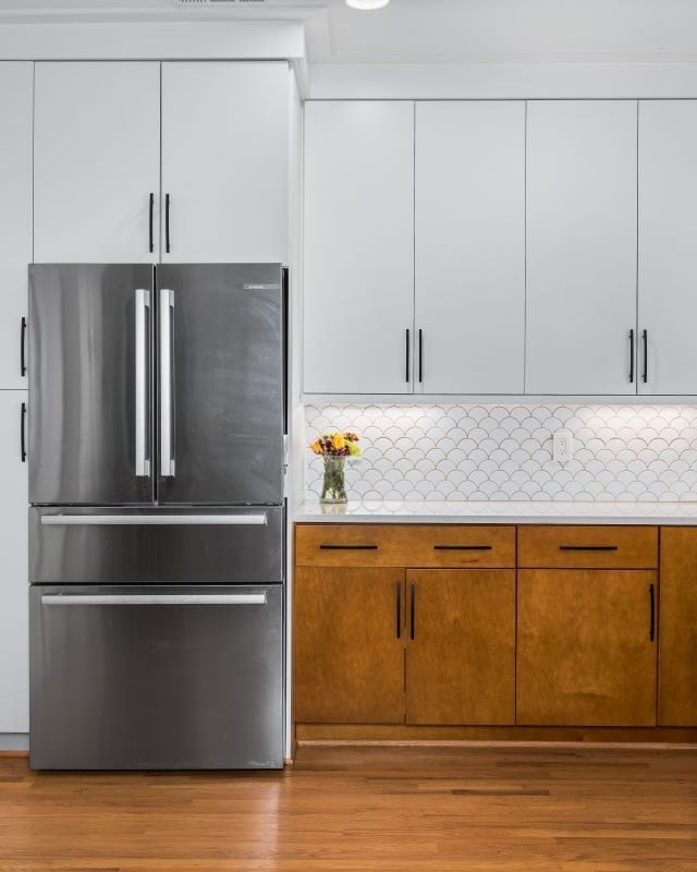 Modern kitchen with white cabinets, wooden accents, and stainless steel appliances.