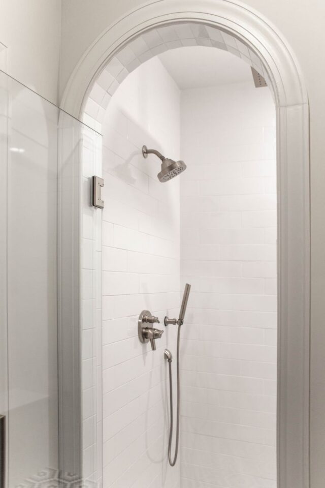 Primary suite bathroom with sleek shower design and white tile walls.