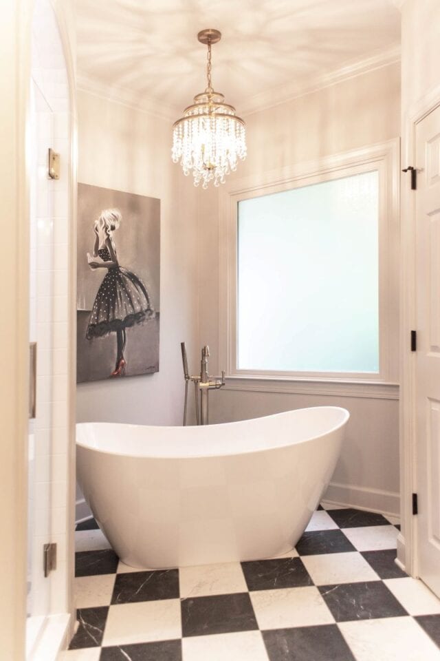 Freestanding bathtub in a luxurious primary bathroom with chandelier and black-and-white checkered f.